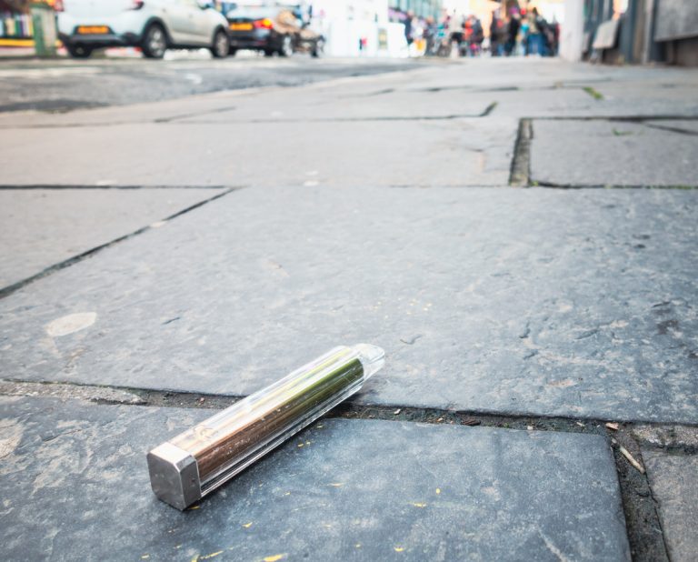 A single use electronic cigarette vape discarded on the pavement of a city.